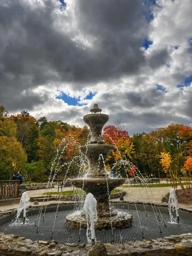 Restored historic belle fountain spraying water in front of autumn trees at Belfountain