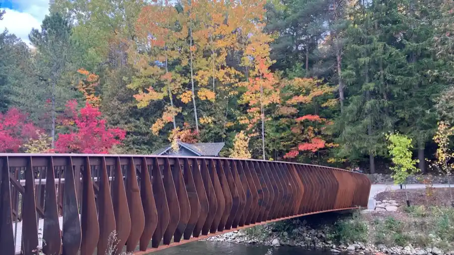Curved rust-coloured pedestrian bridge framed by bright fall foliage at Belfountain