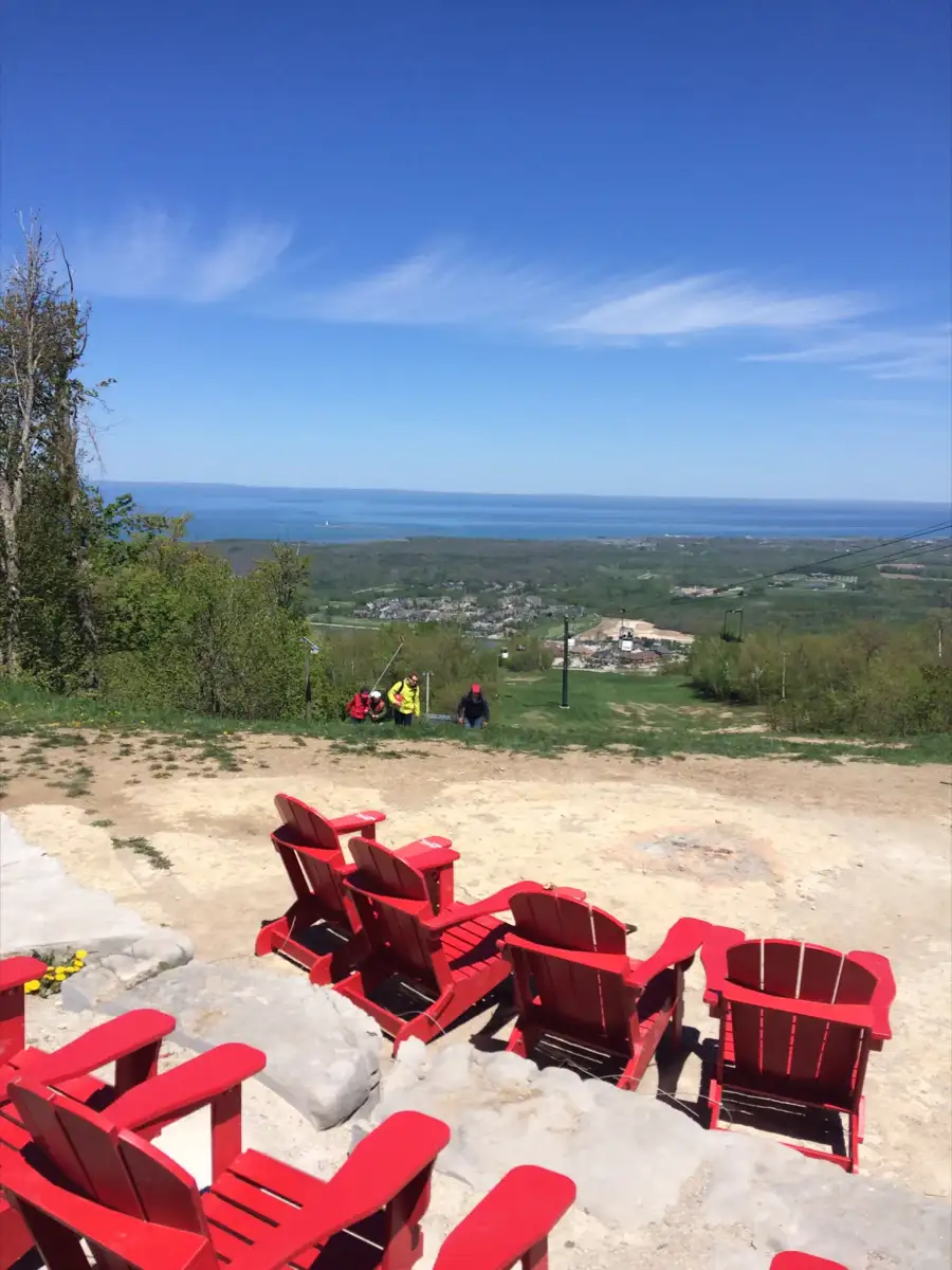 Cadeiras Muskoka vermelhas no topo de Blue Mountain com a Baía de Georgian ao longe