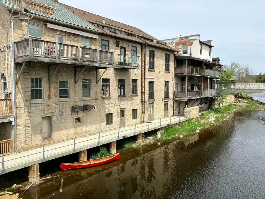 Limestone river buildings with balconies and a red canoe in downtown Elora