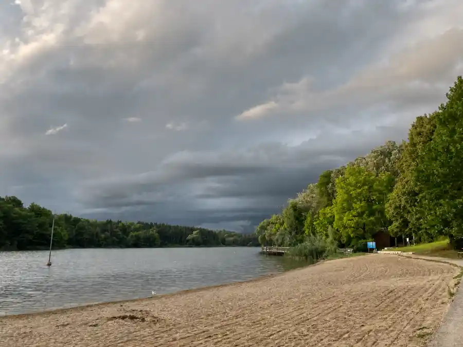 Sandy beach and calm Kelso Lake below a dramatic cloudy sky near Milton Ontario