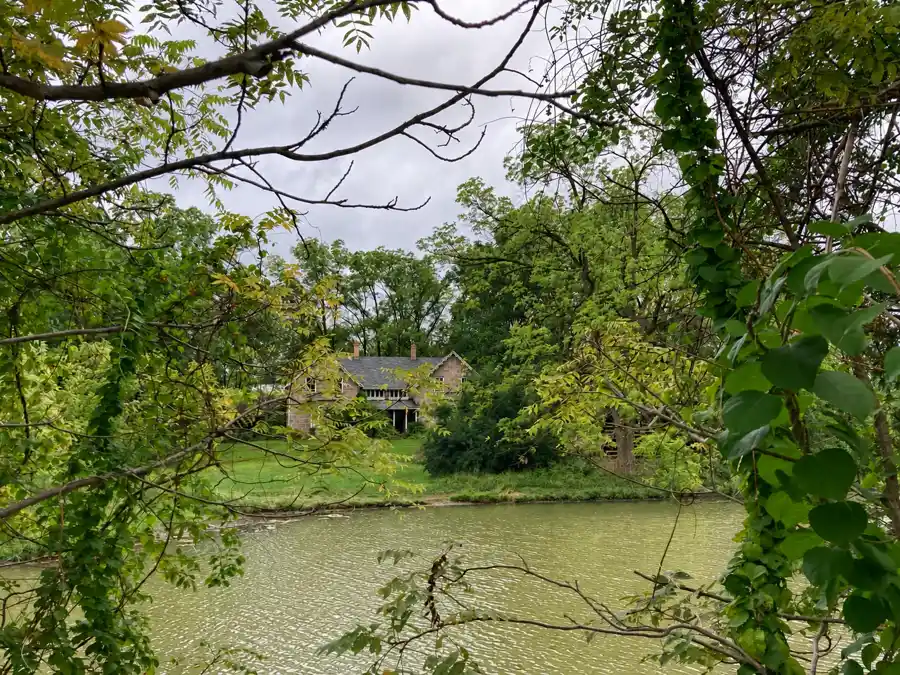 Stone building seen through leafy branches beside quiet water in the Kelso landscape