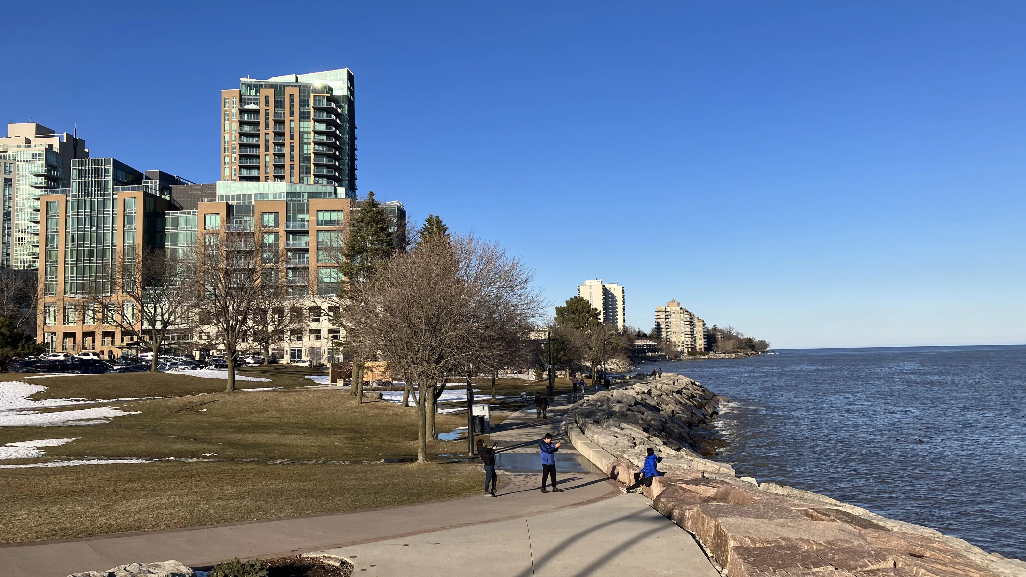 Caminhada à beira-mar de inverno em Burlington ao lado do Lago Ontário com céu azul, rochas costeiras e edifícios no centro da cidade